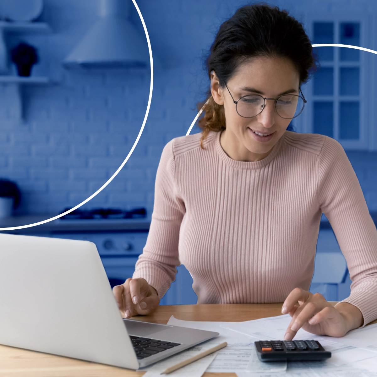 Mulher sorrindo, mexendo e olhando para uma calculadora que está sobre uma mesa com papéis e um notebook